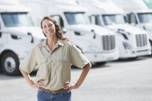 The trucking industry is also trying to recruit more women, who currently make up a small fraction of the workforce., Woman standing in front of semi-trucks